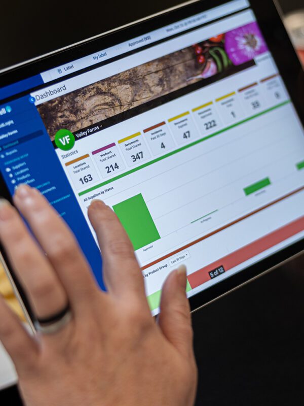 A portable tablet showing the FoodLogiQ Compliance dashboard.