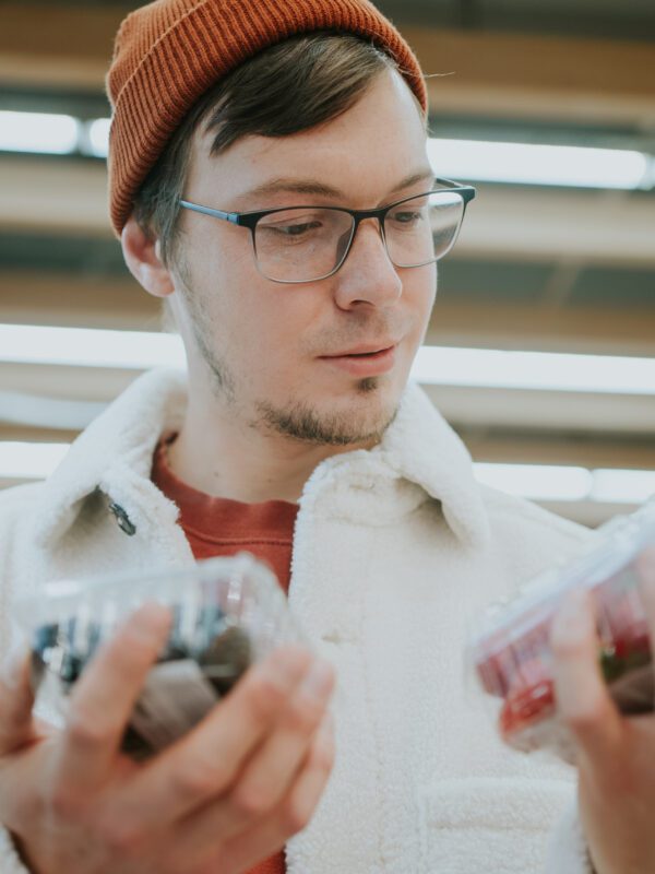 A thoughtful shopper compares containers of fresh berries, making a mindful selection of nutritious options in the produce section. Man Comparing Packs of Berries While Grocery Shopping