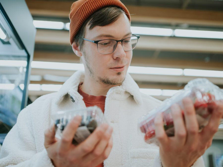 A thoughtful shopper compares containers of fresh berries, making a mindful selection of nutritious options in the produce section. Man Comparing Packs of Berries While Grocery Shopping